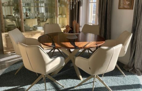 Dieses stilvolle Esszimmer zeigt einen runden, maßgefertigten Holztisch, der von eleganten, cremefarbenen Stühlen umgeben ist. Der Raum wird von einem prächtigen Kronleuchter und einer gläsernen Vitrine akzentuiert, was dem Ambiente einen Hauch von Luxus verleiht. Perfekt für Inneneinrichtungen mit einem Fokus auf hochwertige Holzmöbel.