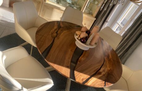 Ein stilvoller runder Esstisch aus hochwertigem Holz mit Epoxidharzelementen zieht alle Blicke auf sich. Umgeben von bequemen, weißen Stühlen wird der Raum zu einem Highlight moderner Wohnkultur. Perfekt für maßgefertigte Eleganz in Ihrem Zuhause.