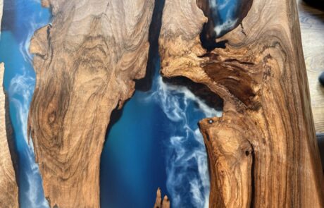 Nahaufnahme eines Rivertable Massivholztisches mit markanter Baumkante und tiefblauem Epoxidharz-River. Weiße, nebelartige Effekte im Harz kontrastieren mit warmen Holztönen und zeigen die natürliche Maserung und Aststruktur.