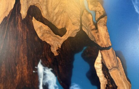 Detailaufnahme einer Massivholz-Tischplatte mit markanter Holzmaserung und leuchtend blauem Epoxidharz-River. Eine weiße, wolkenartige Einschlussstruktur im Harz betont die Naturkante und verleiht dem Rivertable Tiefe