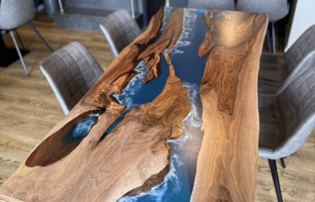 Ein Rivertable als Massivholztisch aus Walnuss mit tiefblauem Epoxidharz-River und sichtbarer Naturkante steht im Essbereich. Die glasglatte Tischplatte und das schlanke Metallgestell bringen moderne Klarheit und betonen die Living Edge Silhouette.