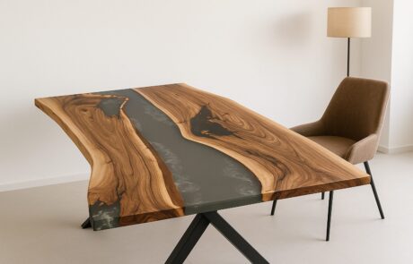 Ein Walnuss Massivholztisch mit dunklem Epoxidharz-River und lebendiger Naturkante steht auf einem schwarzen X-Gestell in einem hellen, minimalistischen Raum. Rechts ist ein brauner Polstersessel und eine Stehlampe zu sehen, die dem Ensemble warme, wohnliche Akzente verleiht.