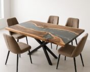 Rechteckiger Massivholztisch mit grauem Epoxidharz-River und sichtbarer Baumkante steht auf schwarzem X-Metallgestell in einem hellen Essbereich. Sechs beige-braune Stühle umgeben den Tisch und betonen die Kombination aus organischer Holzmaserung und modernem Metallfuß.